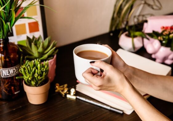 close up of female hands holding coffee cup with coffee and journal on brown desk how to start journaling