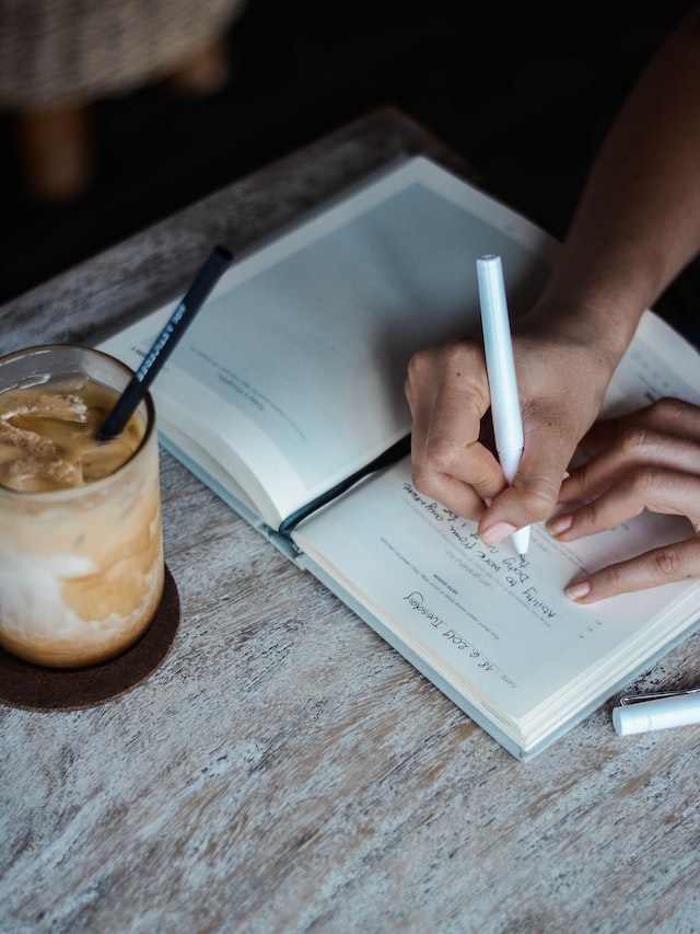 close up of women writing into journal with iced coffee next to journal how to start journaling