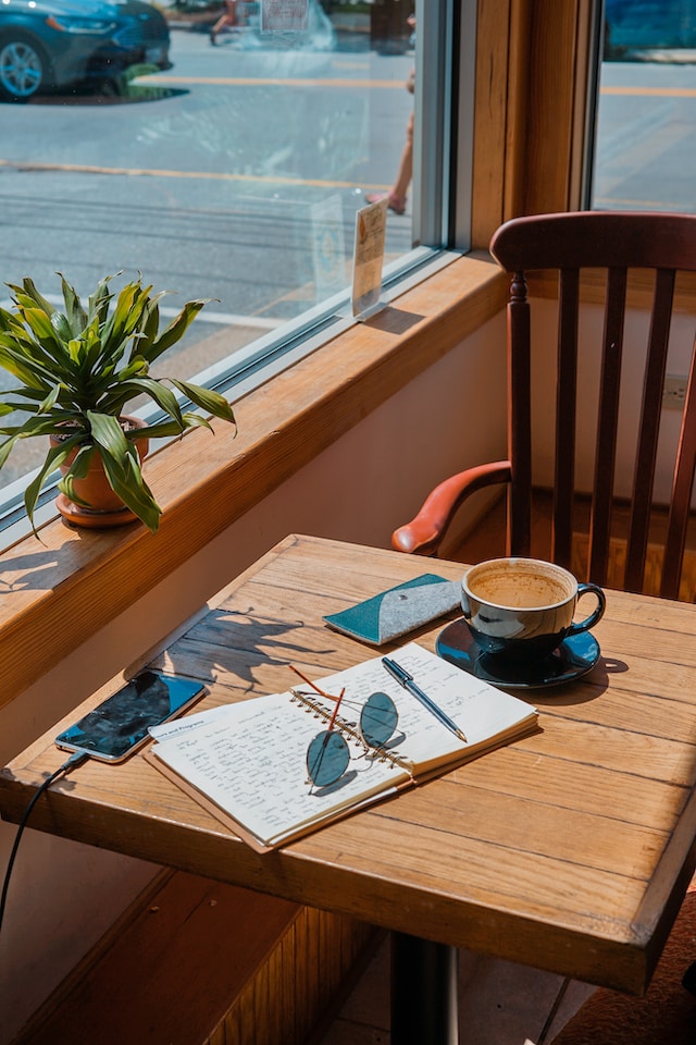 image showing table next to window, on table you see an open journal a cup of coffee and a pair of sunglasses how to start journaling