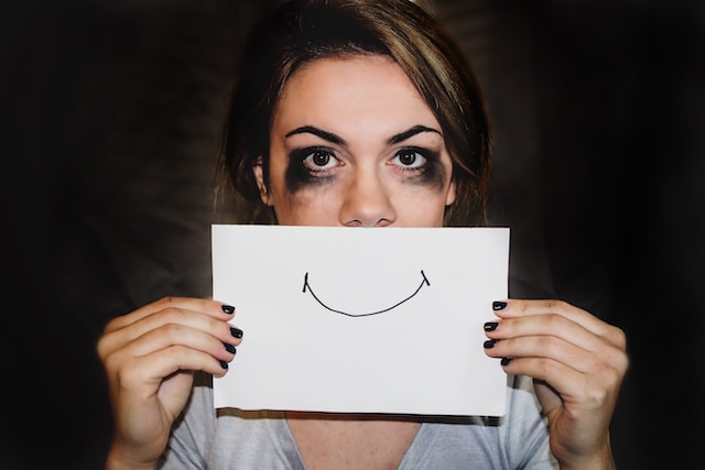 image showing headshot of woman with smudged black eye make-up holding a piece of paper with a smiling mouth in front of her mouth how to start journaling