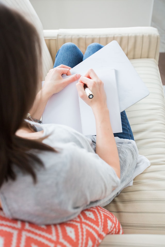 image showing woman from the back writing into journal how to start journaling