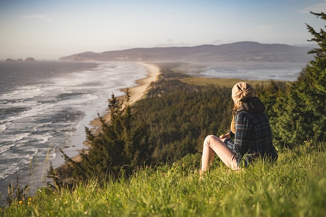 woman sitting on hill in grass looking at seaside how to set healthy boundaries 