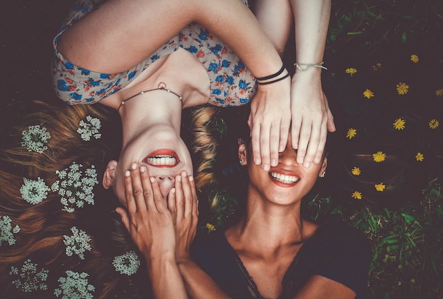 image showing girlfriends lying in grass covering each others eyes and smiling how to cultivate self-love