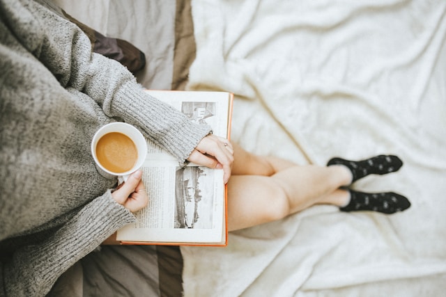 image shows bird perspective of a woman reading a book and holding a cup of tea the blog post is about self love exercises