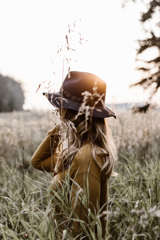 woman with a hat walking in field surrounded by high grass treat yourself ideas benefits
