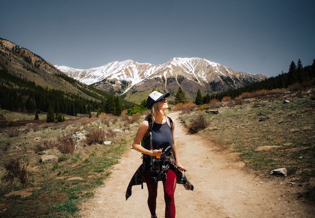 blonde woman wearing hiking gear on hiking trail mountain in the background ways to treat yourself ideas spend time in nature
