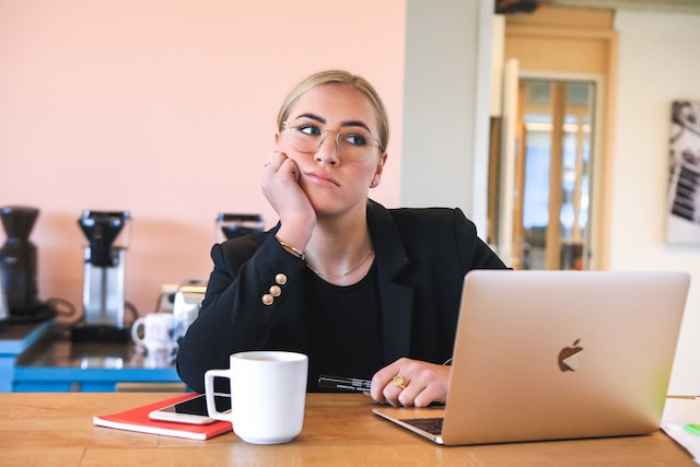 picture showing blonde woman sitting at her desk behind laptop looking bored and demotivated 7 ways to overcome procrastination