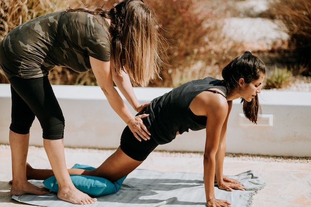 picture showing woman doing yoga and female yoga teacher helping her and adjusting the yoga post first yoga class