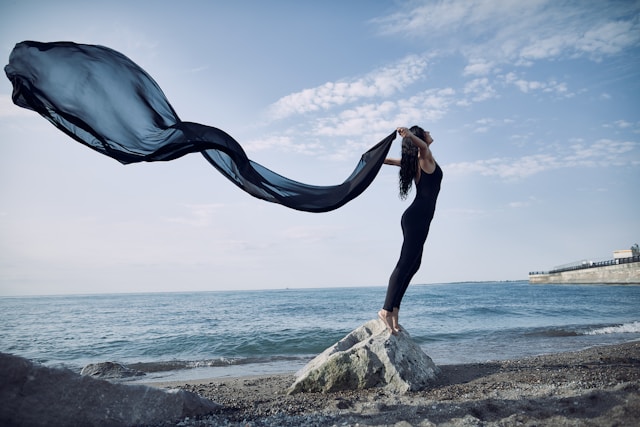 image showing a woman standing on a rock at the seaside she is opening herself up to the future and holds a long scarf in her hands that is flying in the air the blog post is about affirmations for self love