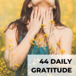 woman with long brown hair standing in field wearing a green dress enjoying a moment of deep gratitude daily gratitude journal prompts