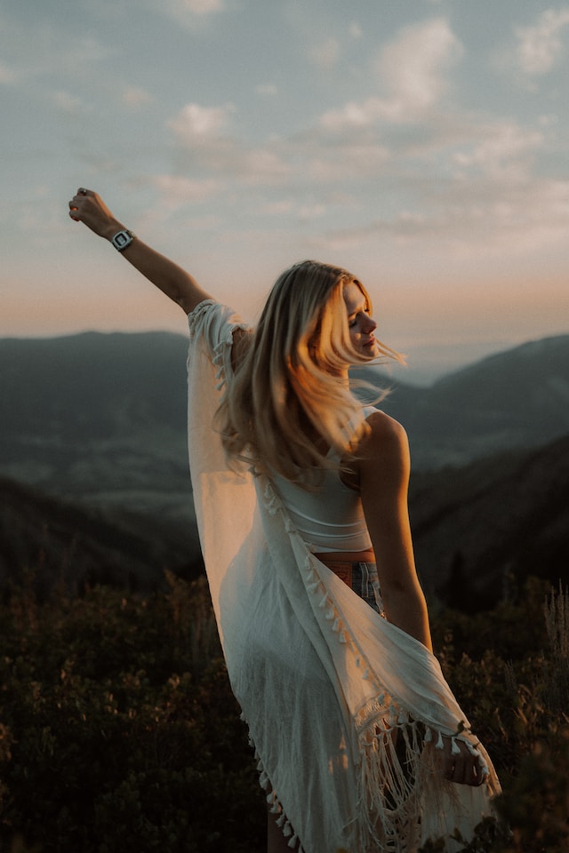 woman with long blonde hair and light white duster coat walking in nature setting enjoying a moment of peace and bliss daily gratitude journal prompts