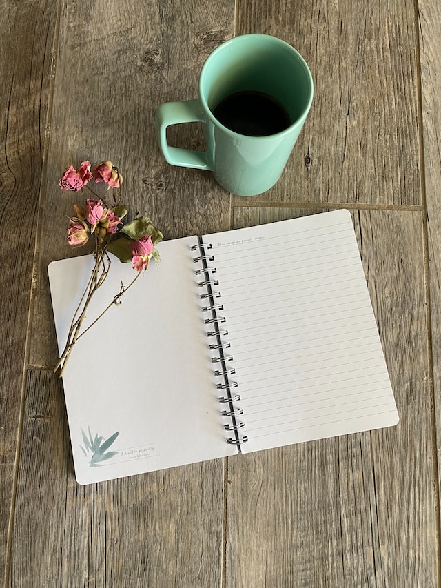 open journal with empty pages placed on wooden table coffee mug in mint green and some flowers as decoration shadow work journal prompts journal