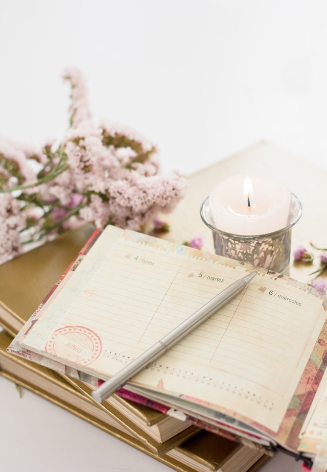 close up of female looking weekly planner on wooden table with white candle and rose flowers as decoration shadow work journal prompts