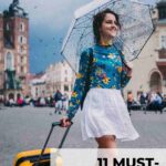 image showing young woman with carry on holding an umbrella walking through city looking excited for her trip long haul flight essentials