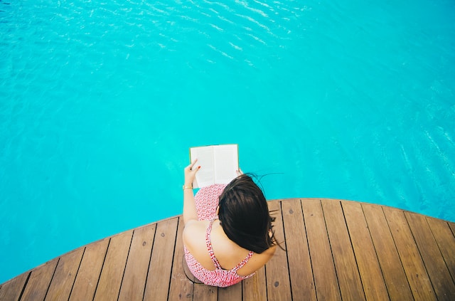 picture showing woman in dress sitting at pool side reading a book image is taken from top perspective ways to relax after work