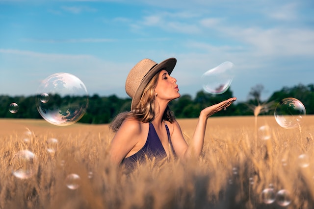 picture showing woman wearing hat standing in field playing with soap bubbles flying around her ways to relax after work
