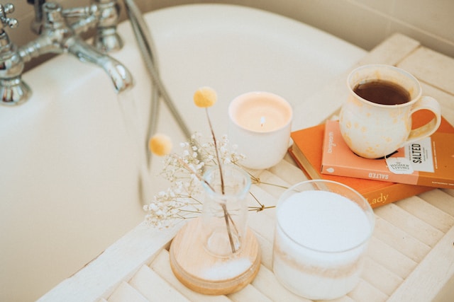 picture showing a bath tub with a cup of tea and a book and flowers and a white candle placed next to it ways to relax after work take a bath
