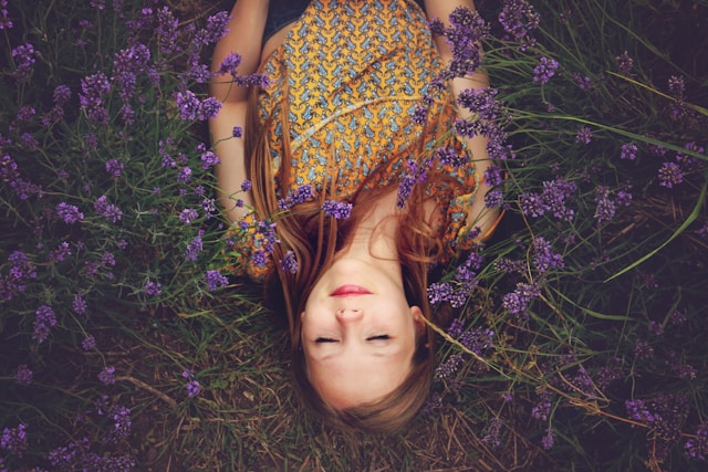 picture shows a woman lying in a flower field enjoying a moment in nature and the blog post is about ways to unwind after a stressful day