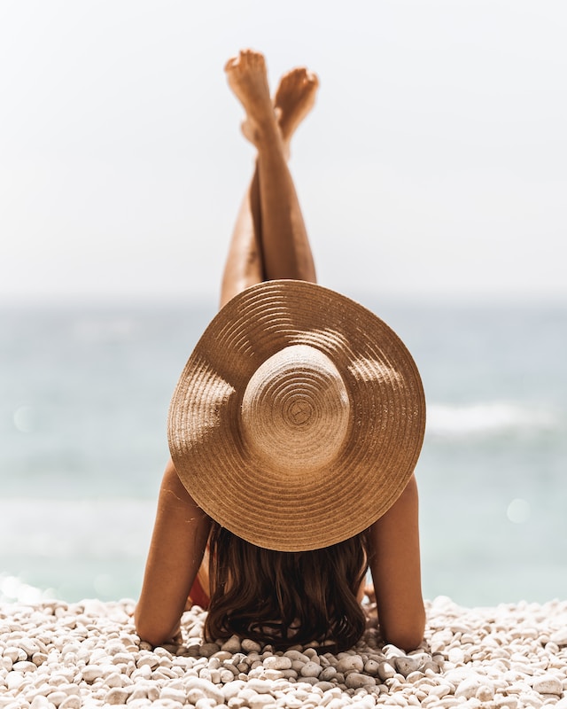 picture shows woman on the beach from the back woman wearing a hat and has long brown hair her legs are pointing up into the air best remote work gadgets