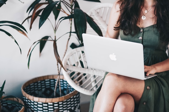 image shows a close up of a woman's upper body and legs sitting on chair dressed in a green dress with her laptop on her lab working blog post features the best remote work gadgets