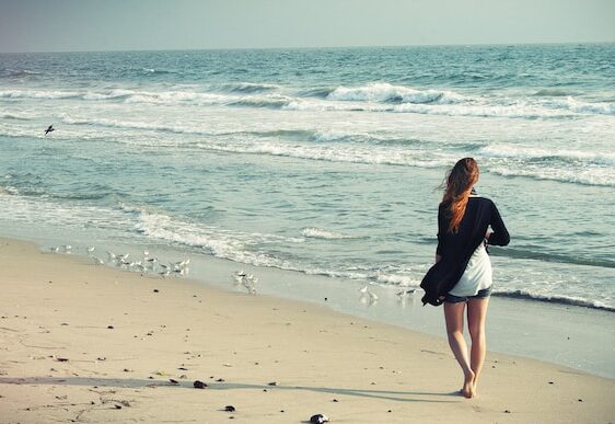 image showing a woman dressed in shorts and a long sleeve top walking along the beach mindfulness and grounding