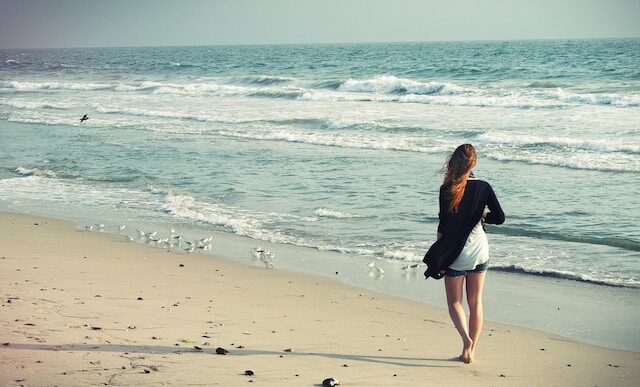 image showing a woman dressed in shorts and a long sleeve top walking along the beach mindfulness and grounding