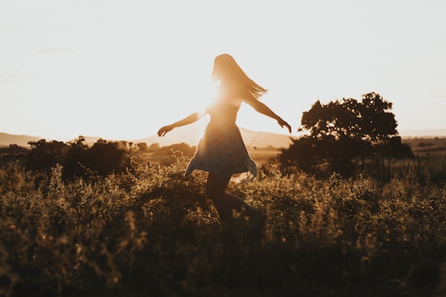 image showing a woman smiling and dancing on a meadow enjoying life and enjoying sunset mindfulness and grounding techniques