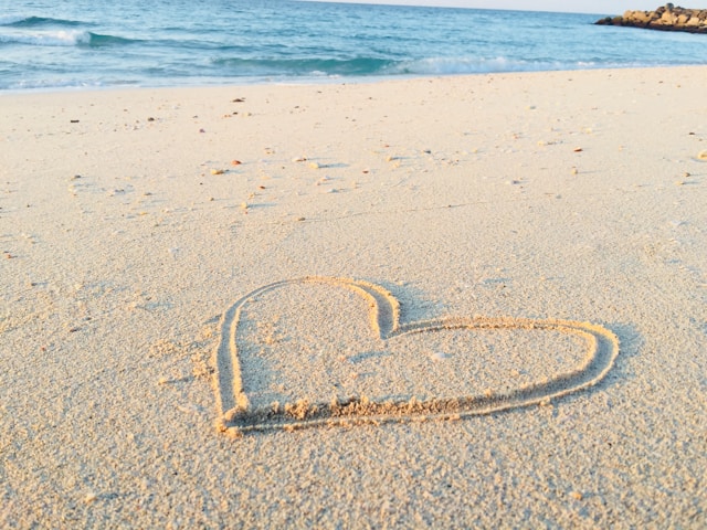 image shows a heart drawn into the sand at the beach with the water in the background blog post is about positive morning affirmations