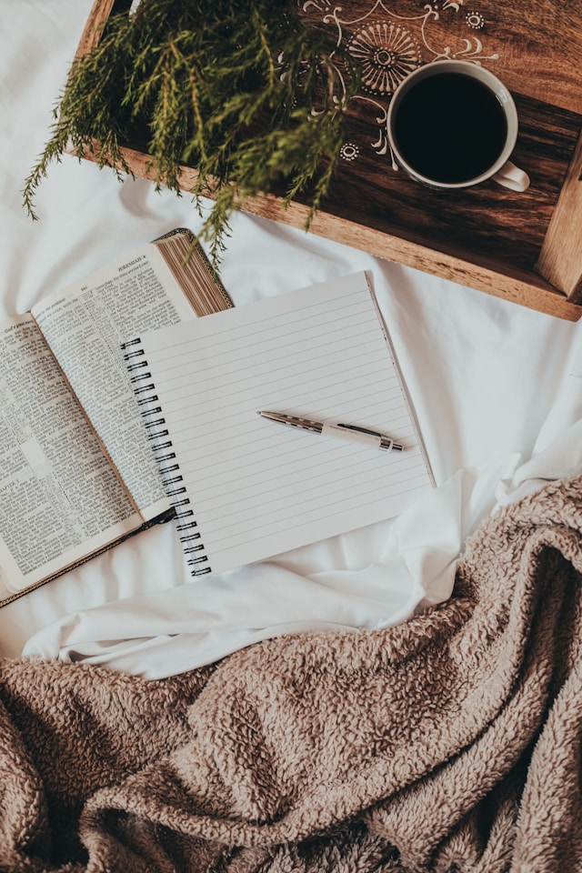 image shows a journal and open book and a pen positioned on a bed with a brown comfy blanket the blog post is about positive morning affirmations