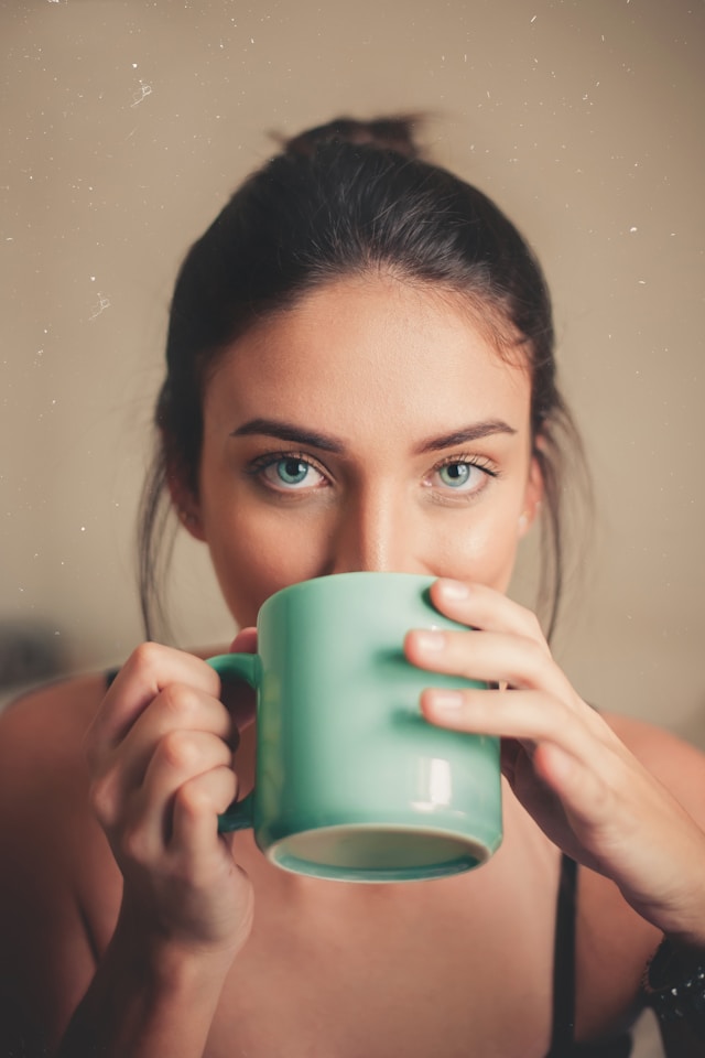 image shows a close up of a woman's head and the woman is drinking coffee out of a green coffee mug the blog post is about positive morning affirmations