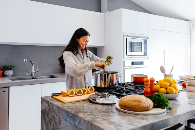 image shows a woman in a nice large modern kitchen and the woman is cooking blog post is about meal prep for busy professionals