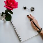 image shows a red rose next to a journal and a close up of a female hand with an ink pen blog post is about self reflection journal prompts for the end of the year