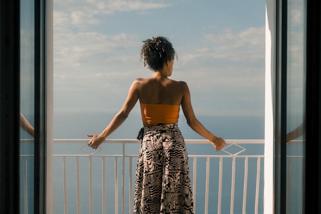 image showing a woman from the back standing on a balcony looking at the sea blog post is about advantages of solo travel