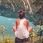 image shows a young woman sitting on a stone overlooking a beautiful river valley blog post is about benefits of solo travel