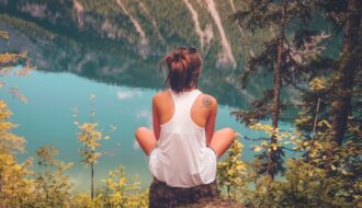 image shows a young woman sitting on a stone overlooking a beautiful river valley blog post is about benefits of solo travel