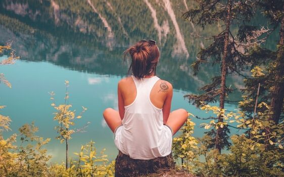 image shows a young woman sitting on a stone overlooking a beautiful river valley blog post is about benefits of solo travel