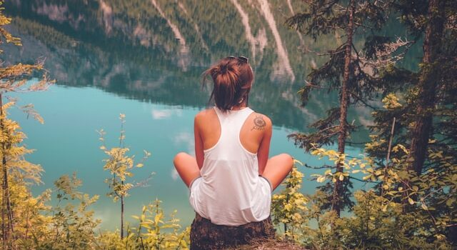 image shows a young woman sitting on a stone overlooking a beautiful river valley blog post is about benefits of solo travel