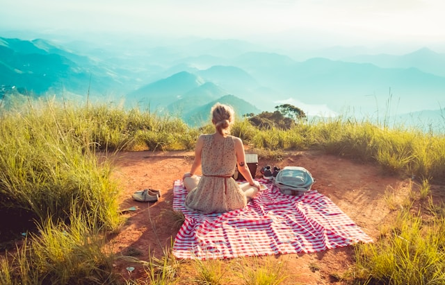 image showing a woman from the back having a picnic on a mountain overlooking a mountain valley blog post is about solo trip benefits