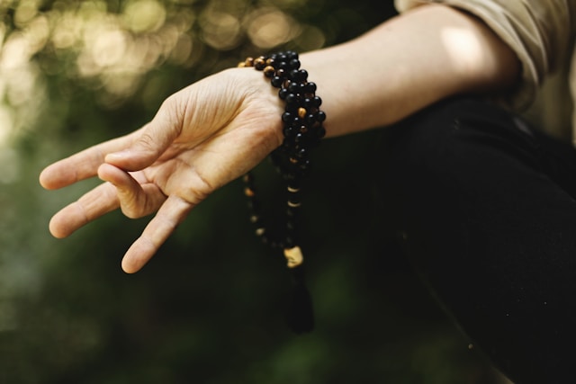 image shows a close up of a hand in meditation pose with a nature setting in the background the blog post is about grounding for anxiety attacks