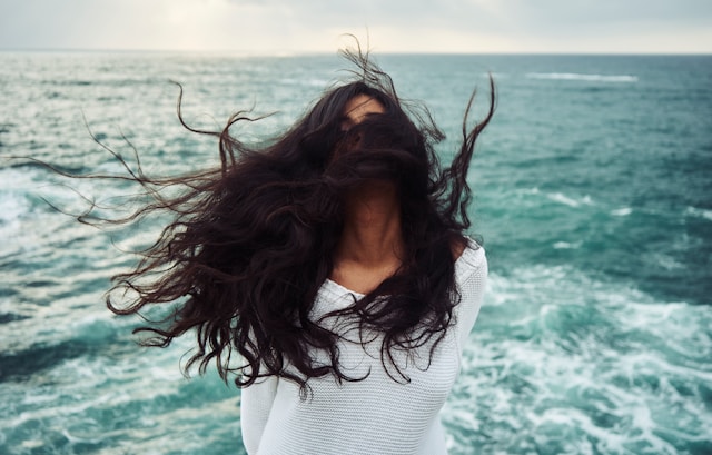 image shows a woman with the seaside in the background and the wind is blowing her hair into her face blog post is about grounding exercises