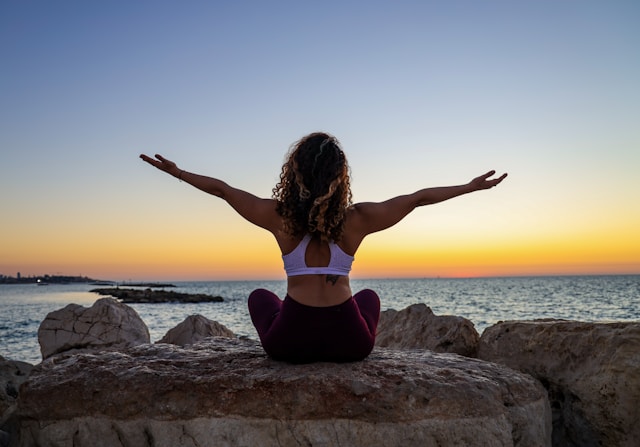 image shows a woman sitting at the beach watching the sunset; she is wearing yoga clothing blog post is about personal growth ideas