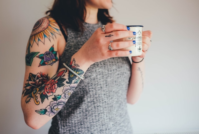 the image shows a close up of the upper body of a woman who holds a cup of coffee and has tattooed arms wearing a grey tank top the blog post is about things to quit to simplify life