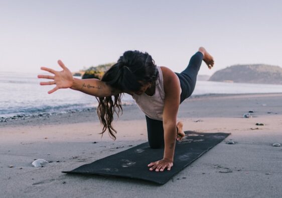 the picture shows a woman on her yoga mat at the beach in an evening setting and the blog post is about relaxing yoga poses for better sleep