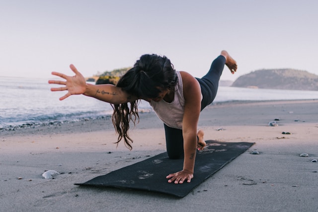 the picture shows a woman on her yoga mat at the beach in an evening setting and the blog post is about relaxing yoga poses for better sleep